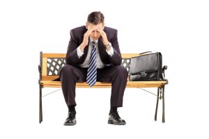 22135079 - disappointed young businessperson sitting on a wooden bench isolated against white background